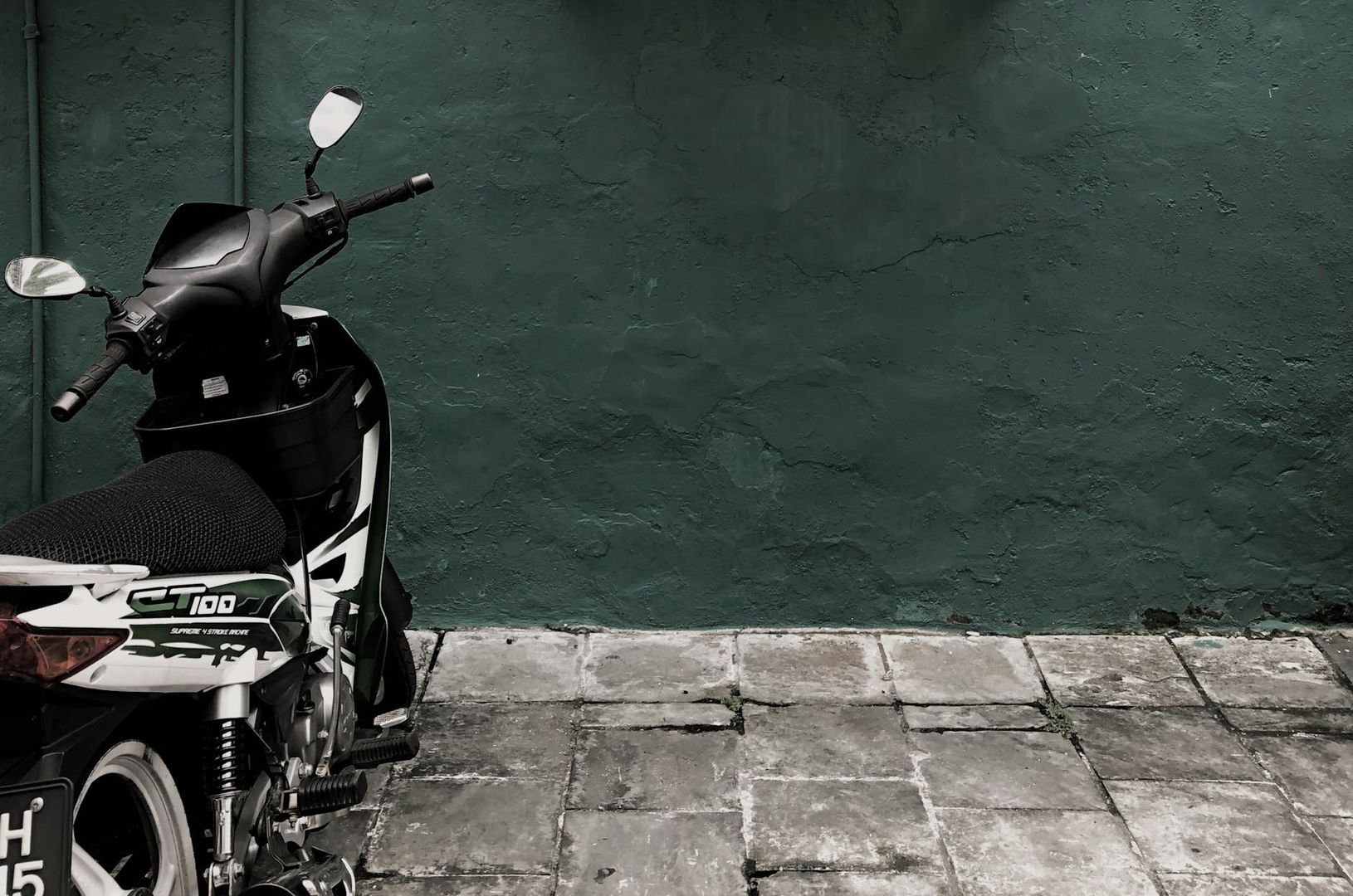 Ein Roller parkt vor einer dunkelgrünen Wand und Pflastersteinen, erinnert an Transport in der Musikbranche.