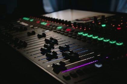 Beleuchtetes Mischpult mit Reglern und farbigen Tasten im dunklen Studio