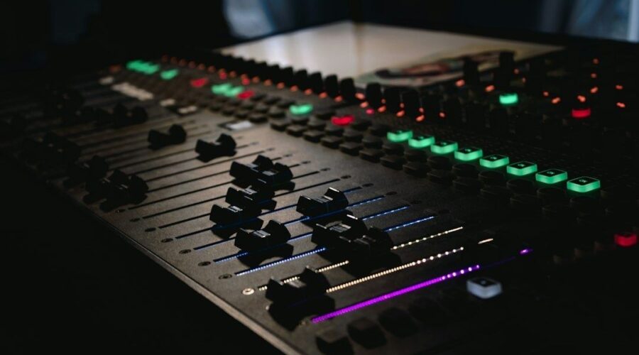 Beleuchtetes Mischpult mit Reglern und farbigen Tasten im dunklen Studio