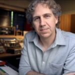 Mann in einem Tonstudio vor analoger Audiotechnik und Mischpult