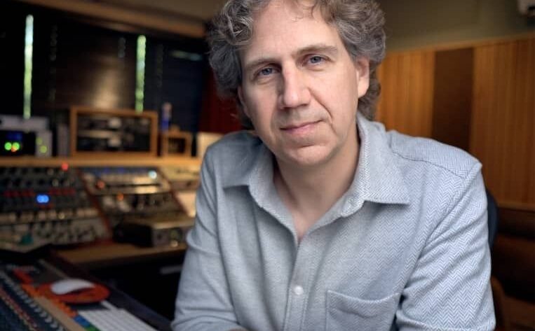 Mann in einem Tonstudio vor analoger Audiotechnik und Mischpult