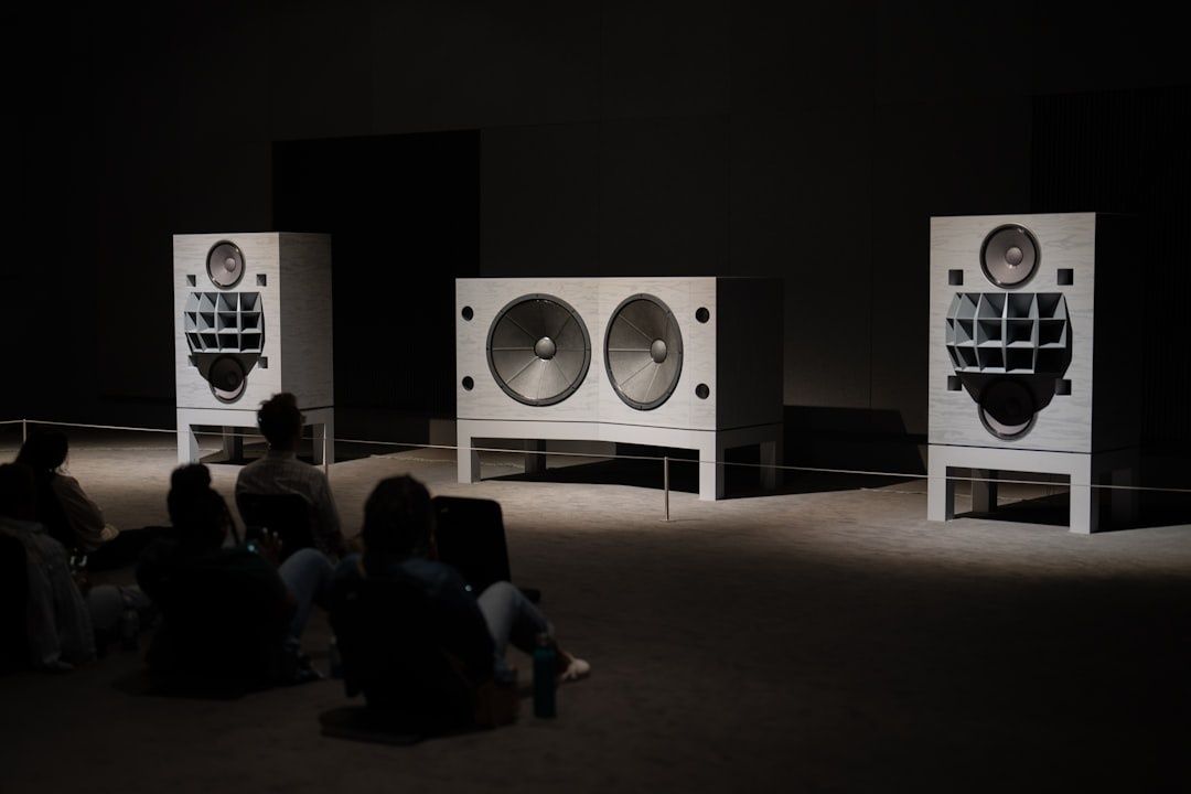 Drei große Lautsprecher in einer abgedunkelten Ausstellung mit sitzendem Publikum