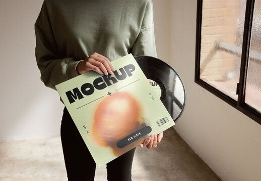 Person hält ein Vinylalbum mit auffälligem Cover vor einer Schallplatte